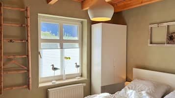 A bedroom with a bed, a wardrobe, a window with blinds, a hanging light fixture, and a wooden ladder.