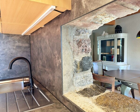 A kitchen with a modern faucet, a stone accent wall, and a dining area with a table and chairs. - defaultName (Glowe)