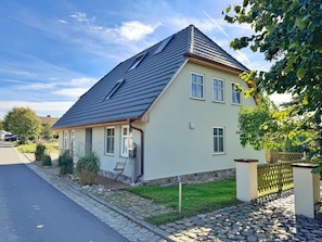 A two-story house with a sloped roof, a front porch, and a stone pathway leading to the entrance. - defaultName (Glowe)
