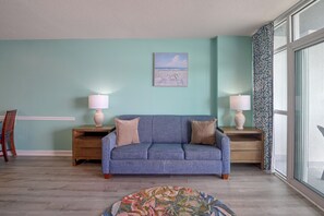 A room with a blue sofa, two nightstands with lamps, a painting on the wall, and a patterned rug. - Ocean-View Dunes Village Condo: Water Park & Pools (Myrtle Beach)