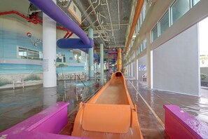An indoor water slide with a clear path, surrounded by walls with safety signs, and a mural of a beach scene. - Ocean-View Dunes Village Condo: Water Park & Pools (Myrtle Beach)