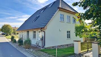 Ein zweigeschossiges Haus mit einem geneigten Dach, einer Veranda und einem Kiesweg, der zum Eingang führt.