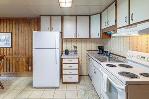 Una cocina compacta con refrigerador, estufa y lavabo. Hay gabinetes de madera y un salpicadero de azulejos.