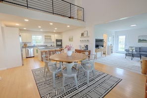 A spacious living area with a dining table, chairs, and a kitchen in the background. - 50-Acre Hilltop Home: Upstate Getaway (Mooers)