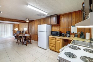 A kitchen with wooden cabinets, a refrigerator, a microwave, a stove, and a dining table with chairs. - Parrot Head Paradise: Lake Access & Pickleball (Clermont)