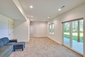 A spacious room with a large sliding glass door leading to a backyard, carpeted floor, and a dark-colored sofa. - Large Deck w/ Views! Brand New Three Rivers Home (Three Rivers)