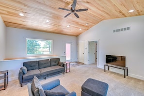 A spacious living area with a ceiling fan, a large window, a flat-screen TV, and a grey sofa. - Large Deck w/ Views! Brand New Three Rivers Home (Three Rivers)