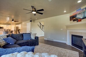 A modern living room with a dark-colored sofa, a white fireplace, and a ceiling fan. - Extended Mtn-View Stay w/ Hot Tub Near Skiing (Mountain Green)