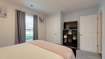 A bedroom with a bed, a dresser, a TV, and a window with curtains.