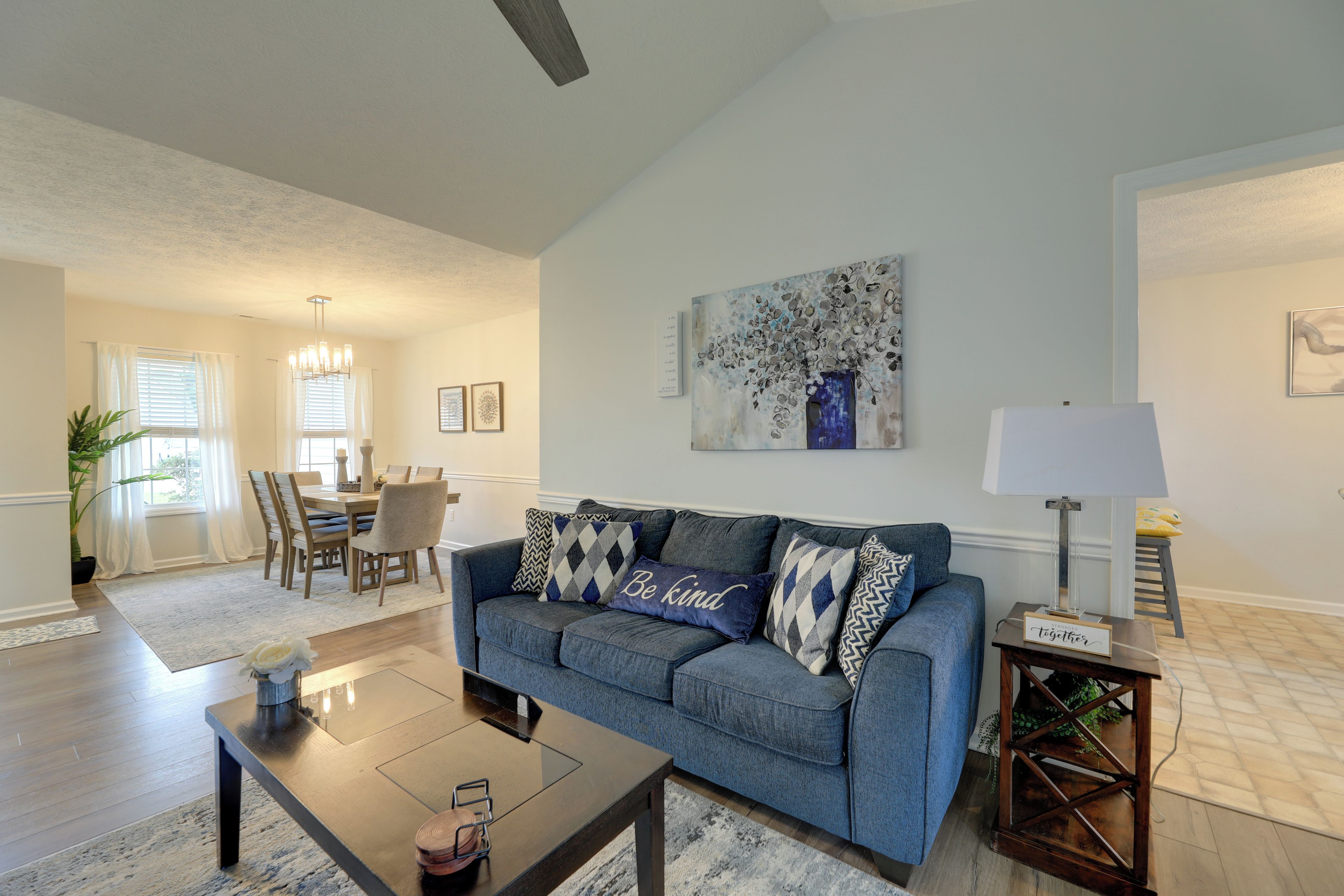 A living room with a blue sofa, a coffee table, a dining area with a table and chairs, and a painting on the wall.