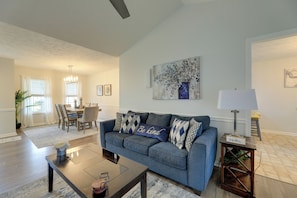 A living room with a blue sofa, a coffee table, a dining area with a table and chairs, and a painting on the wall. - Pet-Friendly Home w/ Fenced Yard Near Cherry Point (Havelock)