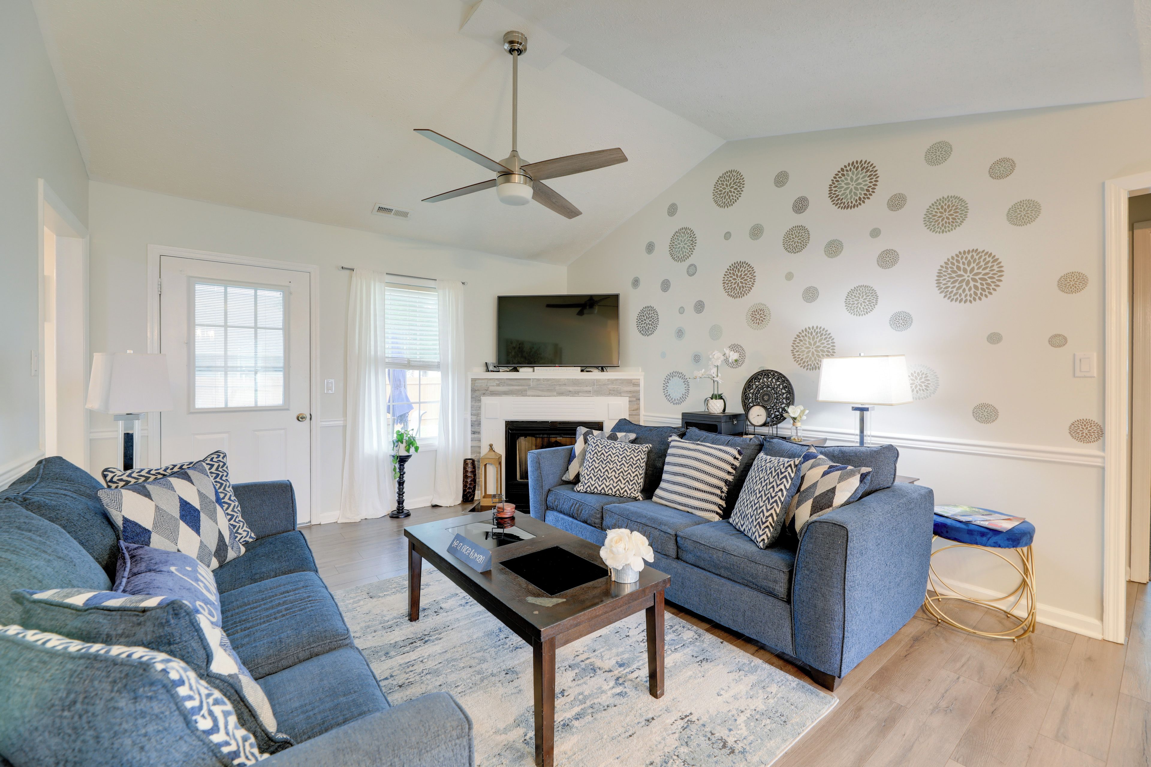 A living room with a blue sofa set, a coffee table, a fireplace, and decorative wall stickers.