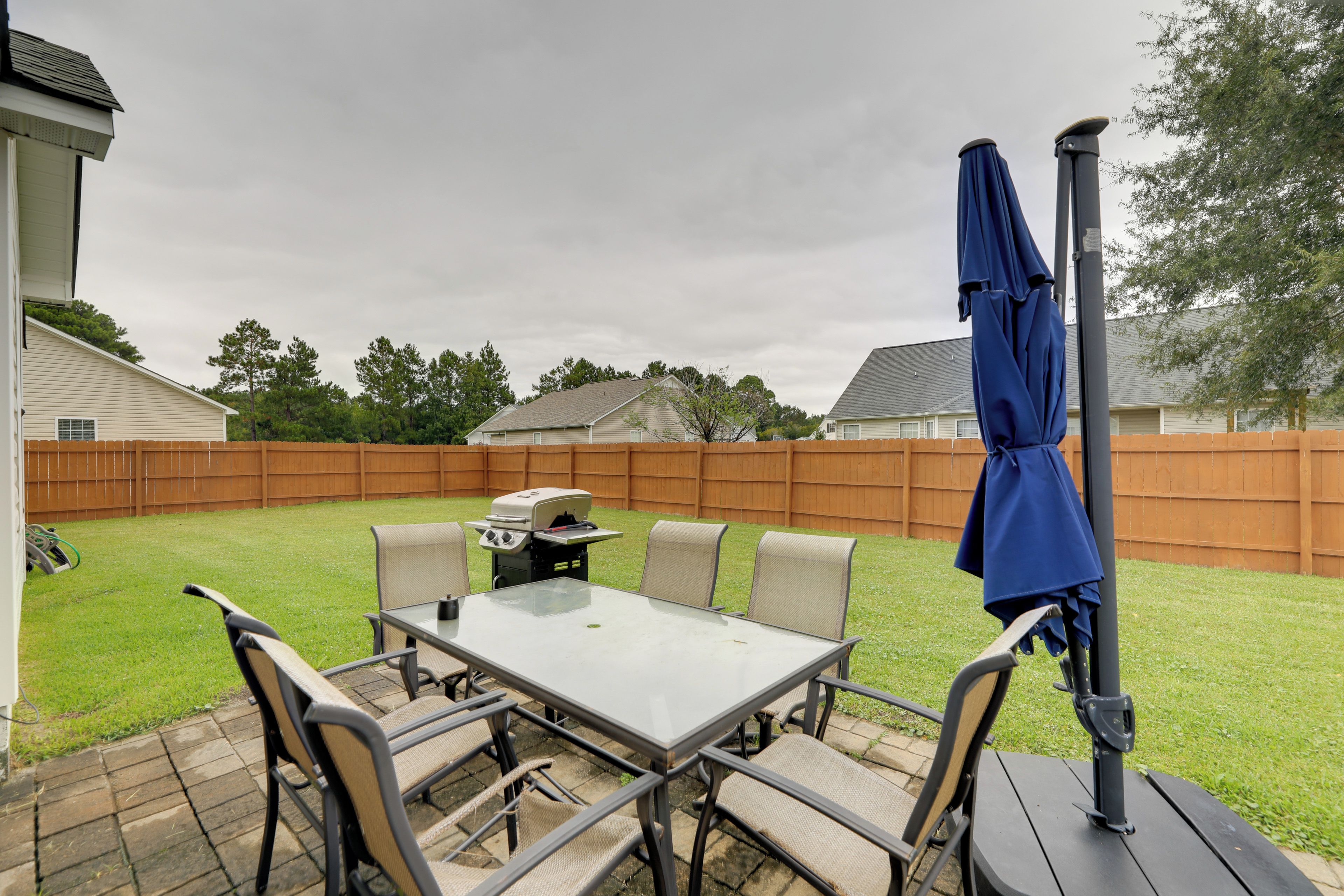 A patio with a table and chairs, a barbecue grill, and a blue umbrella.