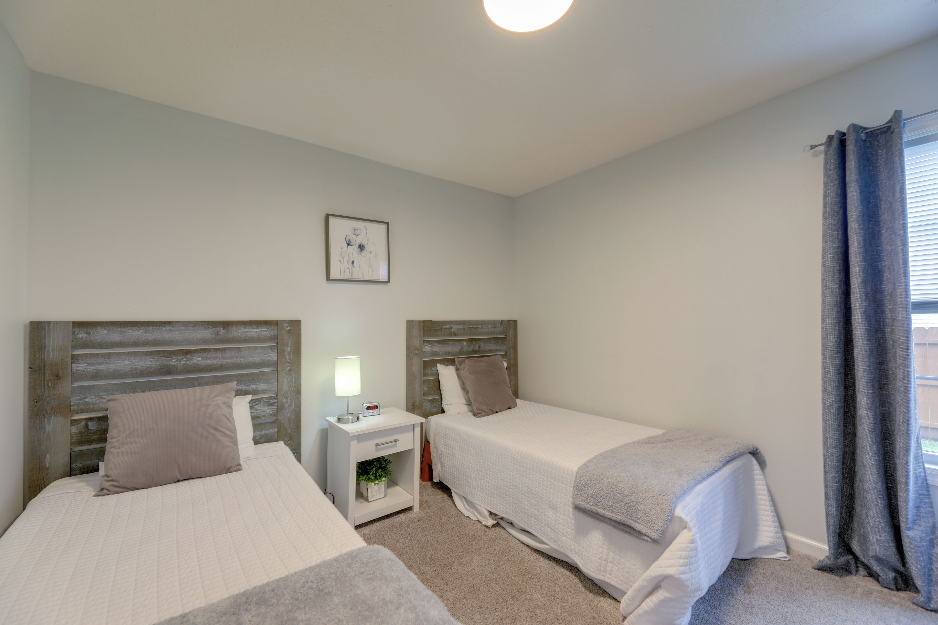 A bedroom with two single beds, a bedside table with a lamp, a small plant, and a picture on the wall.