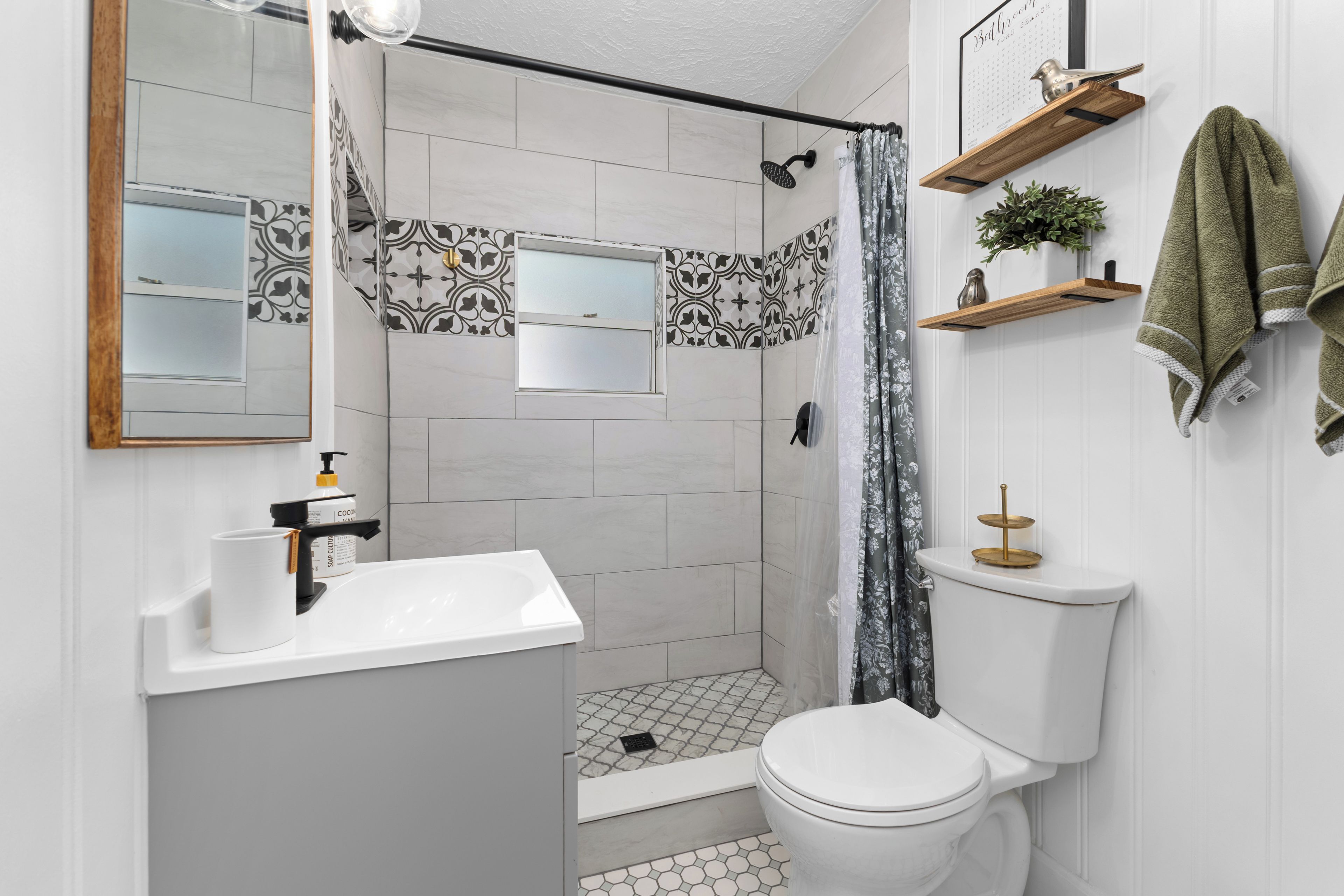 A bathroom with a shower, toilet, sink, and a mirror.