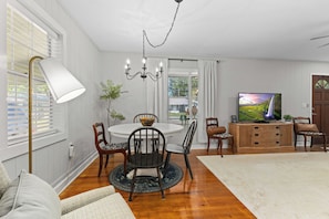 A dining area with a round table, chairs, a chandelier, and a television on a wooden cabinet. - Cute, Cozy & Near Downtown! Updated Home w/ Porch (Live Oak)