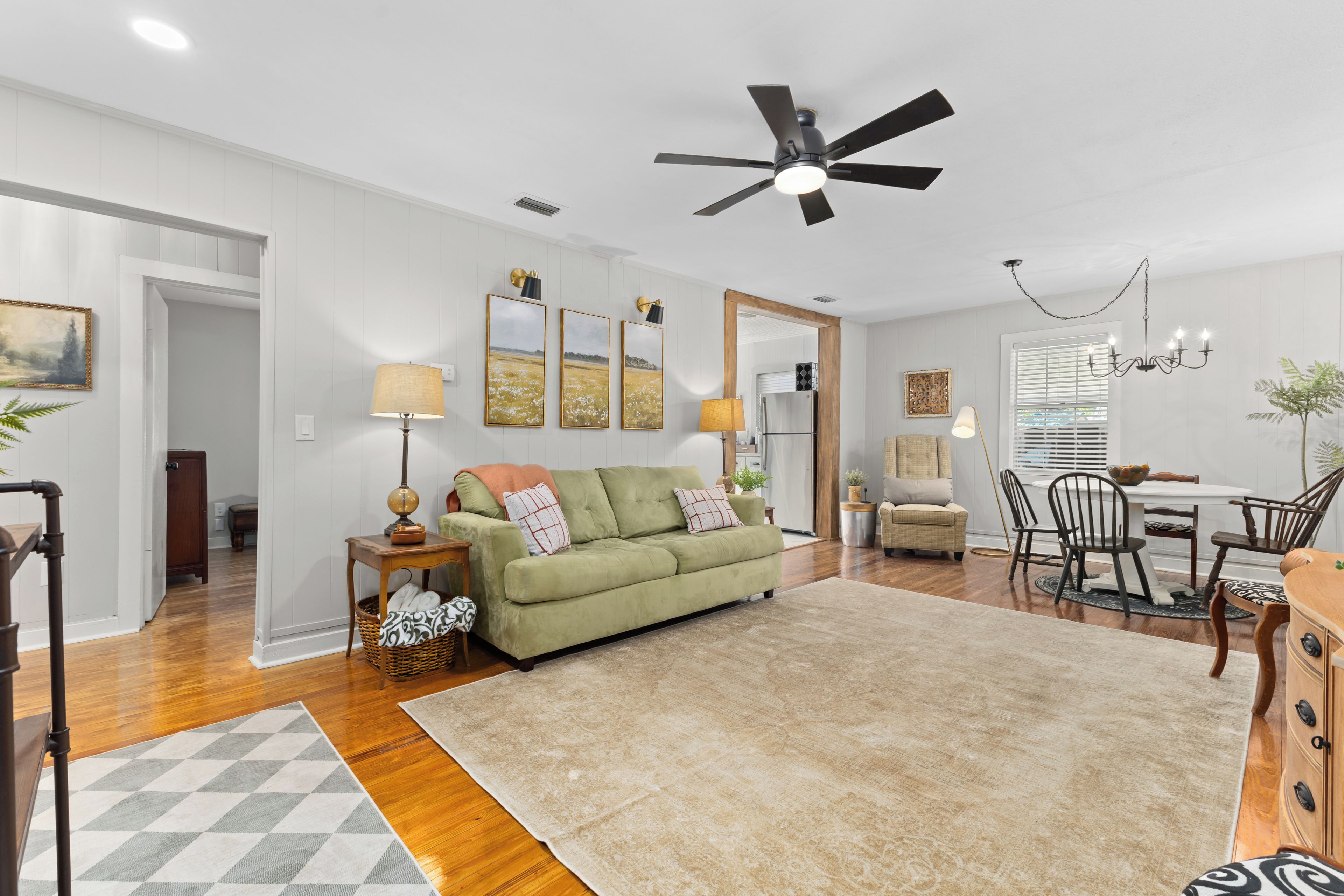 A spacious living room with a green sofa, a dining area with a wooden table and chairs, and a ceiling fan.