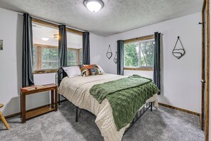 A bedroom with a bed, a bedside table, a window, and a wall-mounted light fixture. - Lakefront Angler's Retreat w/ Dock Access (New Haven)