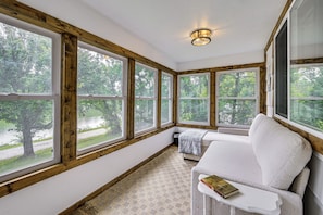 A cozy reading nook with a white sofa, a small table, and a large window with a view of a forest. - Lakefront Angler's Retreat w/ Dock Access (New Haven)
