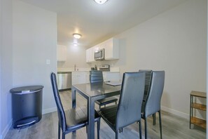 A dining area with a table and chairs, a trash bin, and a kitchen in the background. - Central Lacey Home: 3 Mi to Dtwn Olympia (Lacey)