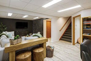A living room with a sofa, a TV, a wooden table, and a staircase. - Spectacular Views & Moose Sightings! Fairbanks Gem (Fairbanks)