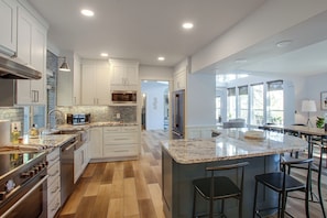 A modern kitchen with white cabinetry, a central island with bar stools, stainless steel appliances, and a view to the dining area. - Liberty Lake Retreat w/ Private Dock (Liberty Lake)