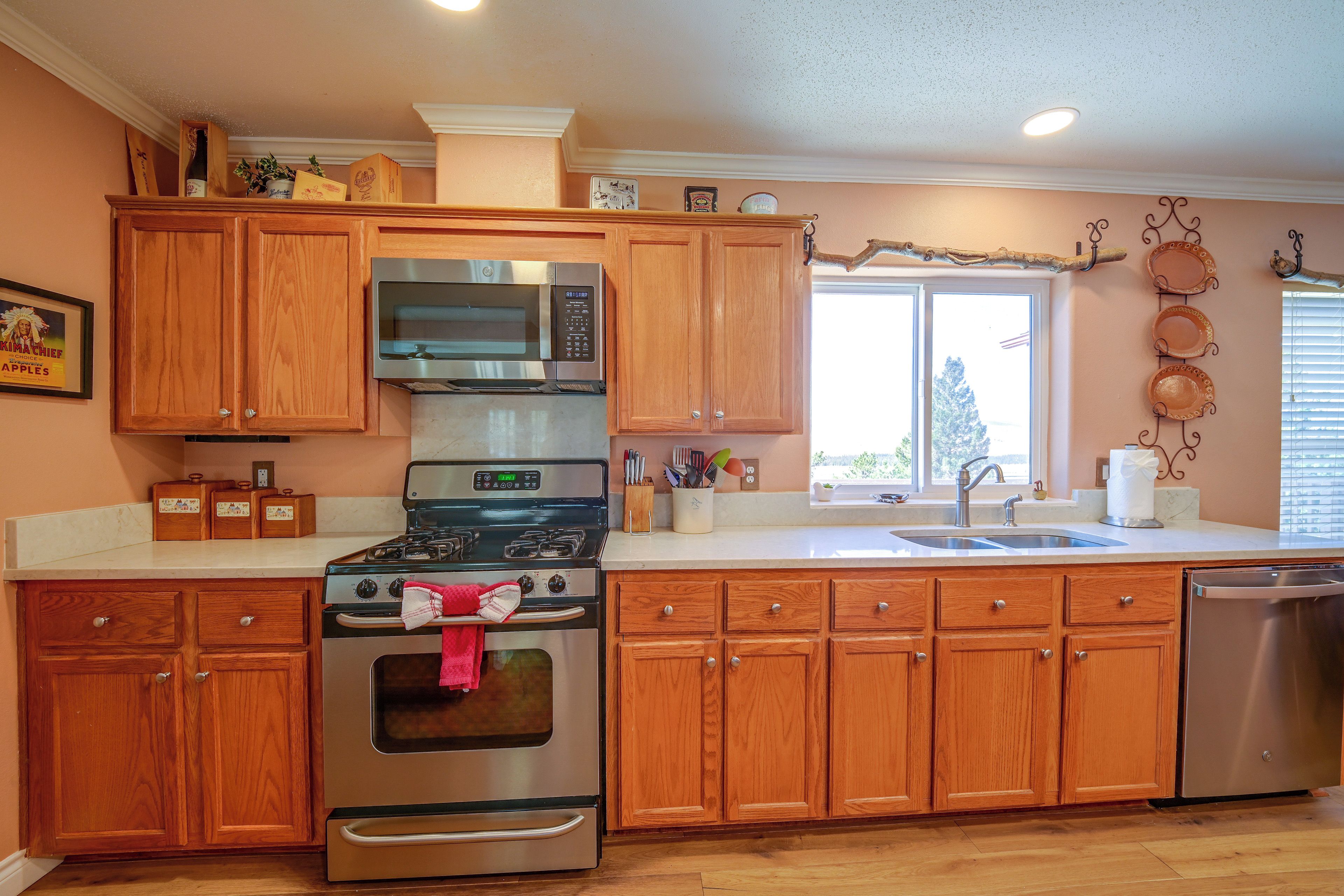 Una cocina con armarios de madera, electrodomésticos de acero inoxidable, una ventana con persianas y un atril decorativo para platos.