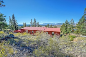 Un edificio rojo con techo metálico, rodeado de árboles y un paisaje montañoso.