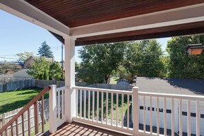 Ein überdachter Balkon mit Holzgeländer, Blick auf einen Garten mit Zaun und ein Haus im Hintergrund.