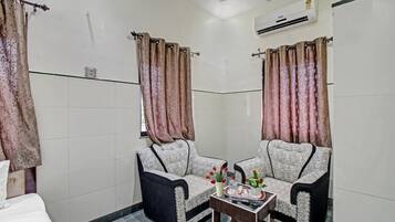 A hotel room with two armchairs, a small table with a tray, and an air conditioning unit on the wall.