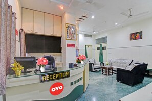 Un área de recepción con mostrador, un sofá y una silla. Hay un cartel que indica los horarios de registro de entrada y salida.