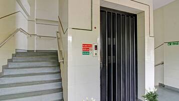 Eine Treppe führt zu einer Tür mit einem Brandschutztürschild und einem digitalen Brandmelder.