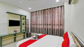 Habitación de hotel con cama, escritorio, televisor y ventana con cortinas.