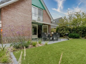 A brick house with a green roof, a patio with outdoor furniture, and a well-maintained lawn. - Holiday Home With 2 Bedrooms (Burgh-Haamstede)