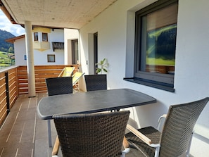 A balcony with a table and chairs, a potted plant, and a window with a view of the mountains. - Marchegg by Interhome (Auffach)