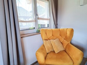 A room with a yellow armchair, a window with curtains, and a view of a building outside. - Marchegg by Interhome (Auffach)