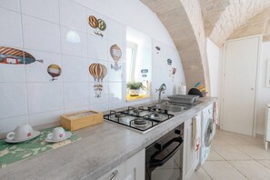 A kitchen with a gas stove, a washing machine, and a tiled backsplash with various designs. - Historic stone vault in NOCI incl  breakfast (Noci)
