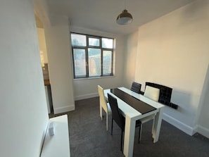 A room with a dining table, chairs, a window with blinds, and a pendant light. - Central Peterborough Home, Garden, Parking, 2 Bed (Peterborough)