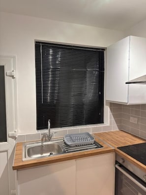 A kitchen with a sink, a window with blinds, a countertop, and a stove. - Central Peterborough Home, Garden, Parking, 2 Bed (Peterborough)