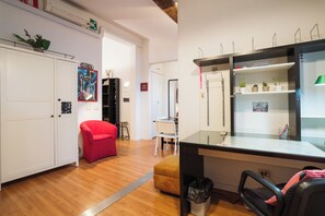 A room with a wooden floor, a red chair, a desk with a computer, a mirror, and a bookshelf. - Borgo Dei Greci Loft (Firenze)