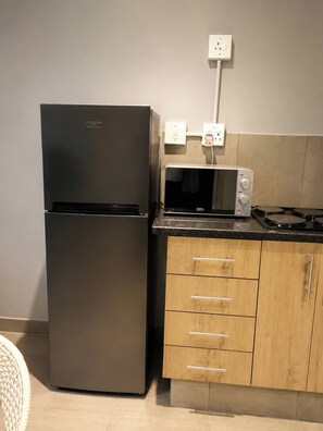 A kitchen with a black refrigerator, a microwave, a gas stove, wooden cabinets, and a white wall socket. - Charming Studio Apartment in Central Randburg (Randburg)