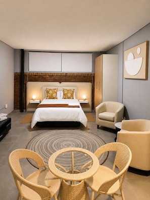 A modern bedroom with a large bed, two bedside tables, a sofa, a round table with chairs, and a wall-mounted artwork. - Charming Studio Apartment in Central Randburg (Randburg)