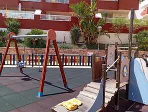 Une aire de jeux avec des balançoires, un toboggan et une structure d’escalade.