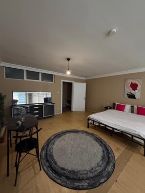 A room with a bed, a dining table with chairs, a small cabinet, a ceiling fan, and a door leading to another room. - Cozy 1-Bedroom Apartment in Pendik, Türkiye (Pendik)