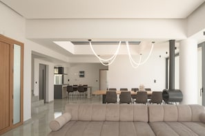 A modern living room with a large sofa, a dining area with a table and chairs, and a kitchen in the background. - Dias Grand Villa - Indoor Outdoor Pools (Mylopotamos)