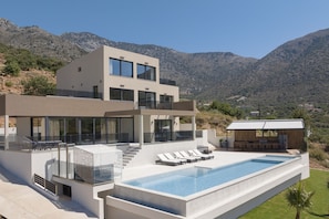 A modern two-story house with a swimming pool, outdoor seating, and a view of the mountains. - Dias Grand Villa - Indoor Outdoor Pools (Mylopotamos)