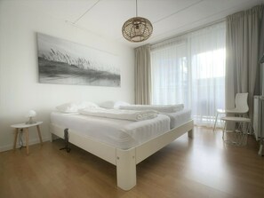 Ein modernes Schlafzimmer mit einem großen Bett, einem Nachttisch, einem Sessel und einem großen Fenster mit Vorhängen.