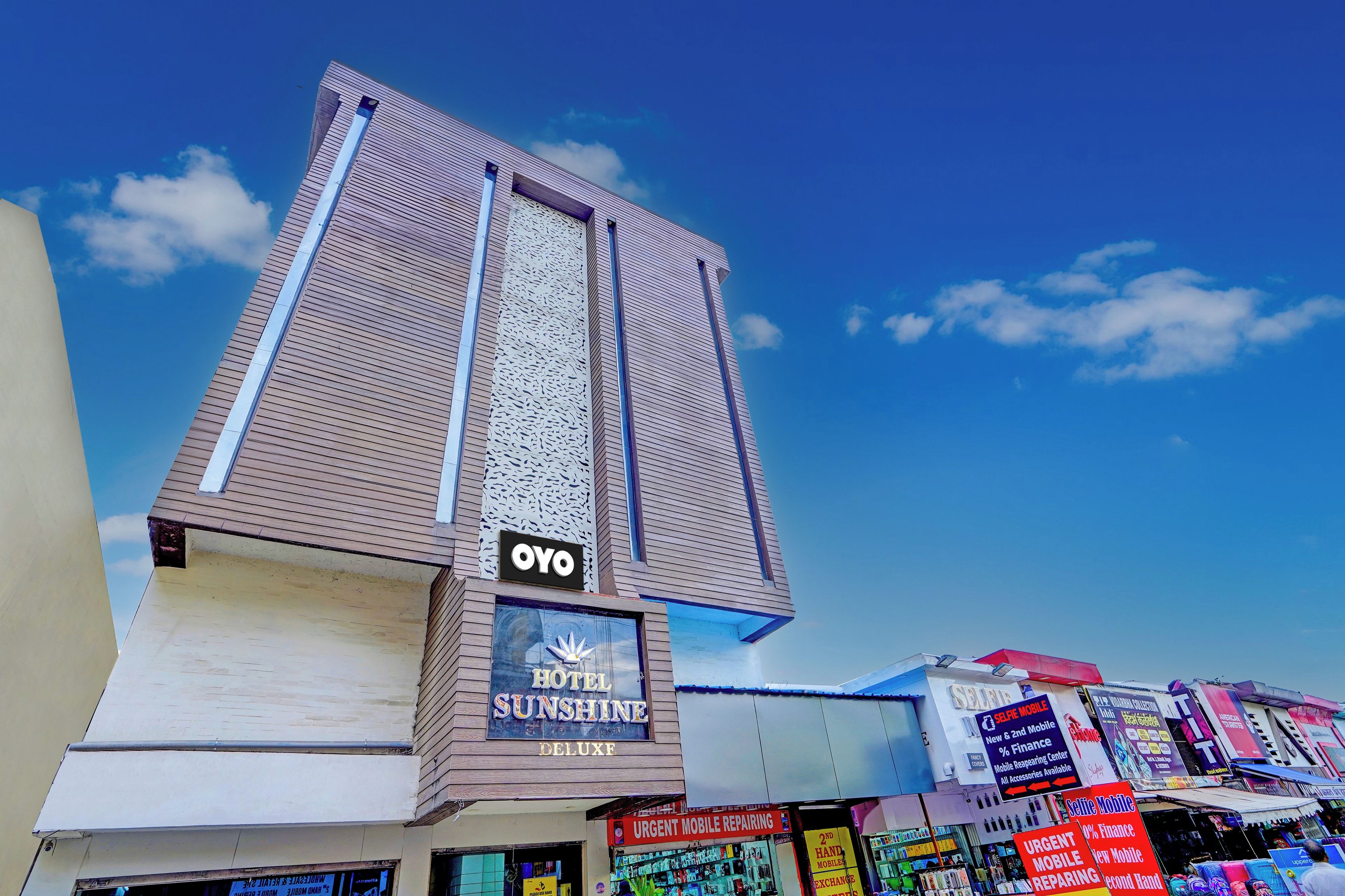 Un hotel llamado 'OYO' con un letrero que indica 'HOTEL SUNSHINE DELUXF' y una tienda de reparación móvil '2ND MOBILE REPAIRING'.