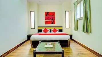 Habitación de hotel con cama, mesita de noche, ventana con cortinas y una pared decorada con tres cuadros rojos y negros.