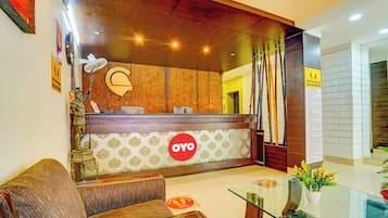 Zona de recepción de un hotel con un mostrador de madera, un sofá y una mesa de vidrio con un florero.